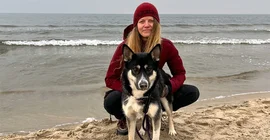 Foto einer jungen Frau, am Strand hockend mit ihrem Hund