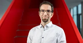 Prof. Dr. Tim Dietrich stands in front of a red staircase.
