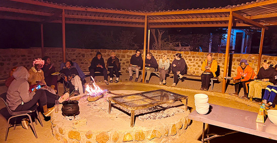 Menschen sitzen am Abend um ein Feuer