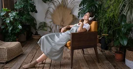 Frau sitzt in einem Stuhl und hört mit Kopfhörern Musik.