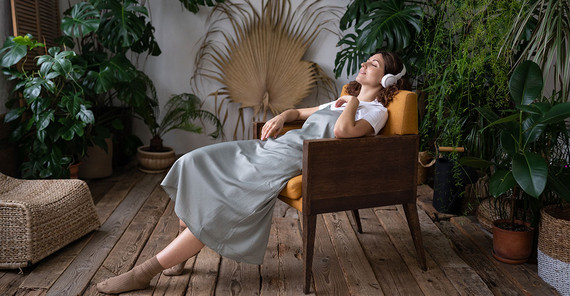 Frau sitzt in einem Stuhl und hört mit Kopfhörern Musik.