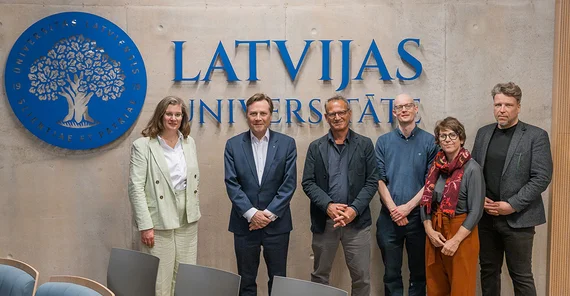 Delegation der Uni Potsdam mit dem Direktor des Deutschland-Zentrums Raivis Bičevskis vor Wand mit Logo der Universität Lettlands.