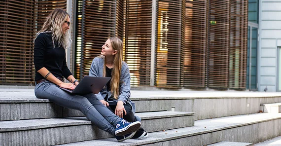 Zwei junge Frauen sitzen auf einer Treppe und unterhalten sich.