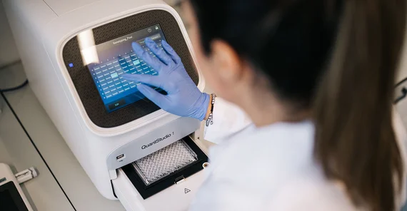 Blick über die Schulter einer Person im Labor. Sie tippt am Display einer Maschine.