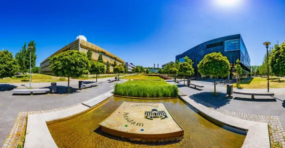 Aufnahme von zwei Gebäuden, in der Mitte ein Wasserspiel