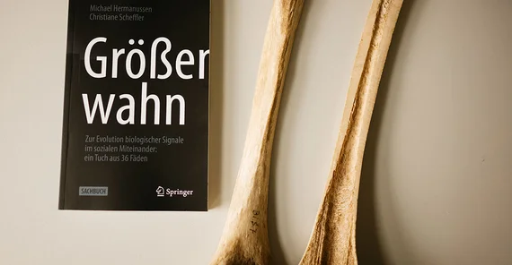 Close-up vom Buch "Größenwahn" und zwei Hälften eines der Länge nach aufgeschnittenen (Oberschenkel)Knochens.