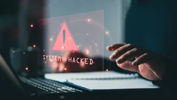 Laptop mit Schriftzug "System hacked" und eine Hand auf der Tastatur