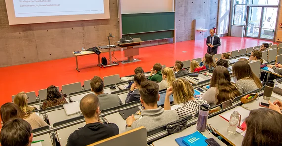 Blick in einen Hörsaal von hinten über die Köpfe der Studierenden auf den vortragenden Wissenschaftler