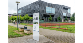 Vorn die Informationstafel, im Hintergrund der schwarze Kubus der Bibliothek