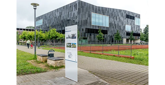 Vorn die Informationstafel, im Hintergrund der schwarze Kubus der Bibliothek