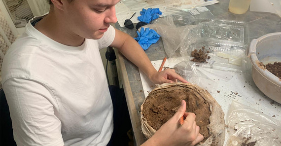 Eine Person legt mit einem kleinen Werkzeug Elemente einer Aschenurne frei.