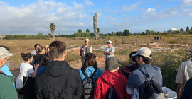 Gruppe von Menschen stehen vor einer Ausgrabungsstätte, während ihnen ein Mann etwas erklärt