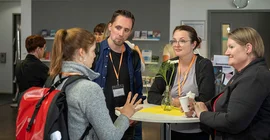 Vier Personen sthen an einem Stehtisch und Reden miteinander