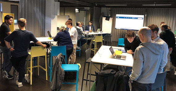 Menschen stehen an Tischen in einem Raum und reden miteinander