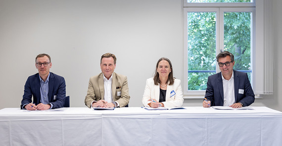 Vier Personen sitzen an einem Tisch und schauen in die Kamera