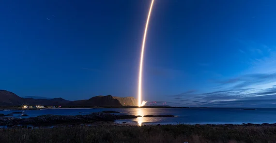 Illuminated rocket launch from a distance in stark contrast to dark night sky.