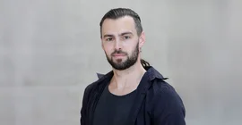 Steffen Hagemann im Porträt vor einer grauen Betonwand am Campus Griebnitzsee.