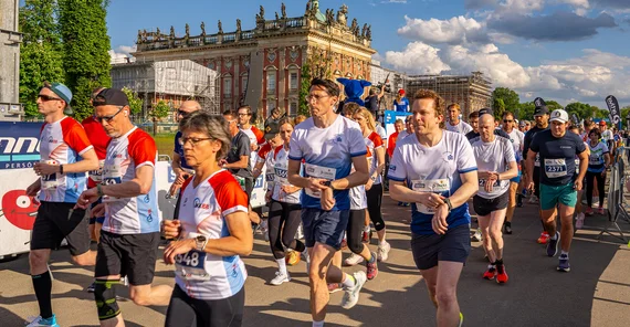 Sportbegeisterte Menschen starten zum Firmenlauf in großer Gruppe.