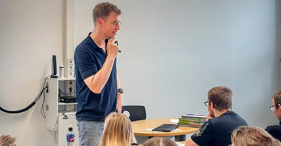 Ein Mann steht in einem Klassenraum und erklärt Schülerinnen und Schülern etwas