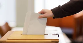Eine hand wirft einen Wahlzettel in eine Wahlurne.