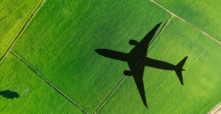 Bird's-eye view of green fields. The shadow of an airplane flying overhead is cast upon them.