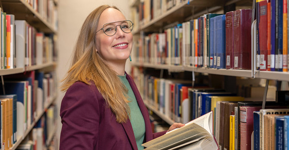 Porträt einer Frau, die im Gang einer Bibliothek steht