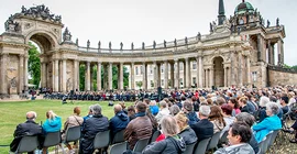 Gäste sitzen vor den Kolonnaden und verfolgen das Programm