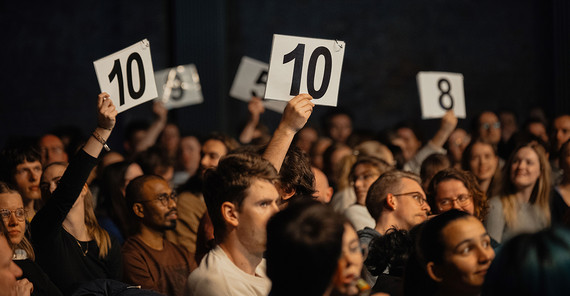 Menschen bei einer Veranstaltung, von denen einige Schilder mit Zahlen zur Abstimmung hochhalten