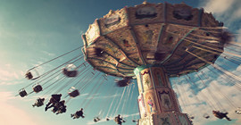 Bild: Adobe Stock/ Tom Bayer. Auf dem Bild ist ein fahrendes Kettenkarussel abgebildet.