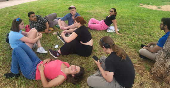 Teilnehmende sitzen und liegen auf einer grünen Wiese im urbanen Raum.